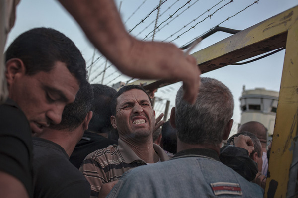Seorang pria Palestina meringis karena kesakitan ketika berdesakkan di gerbang yang menjadi satu-satunya pintu masuk di pos pemeriksaan Eyal. Gerbang ini sering tiba-tiba menutup tanpa pemberitahuan. foto: Daniel Tepper/Electronic Intifada