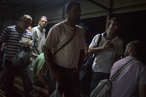 Dengan makanan, kopi dan rokok di tangan, pria-pria Palestina berjalan ke arah jalur khusus di pos pemeriksaan Eyal. foto: Daniel Tepper/EI