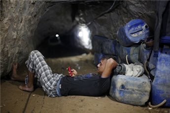 Seorang pekerja terowongan Gaza berbaring sambil mengamati telepon genggamnya. foto: Maan News