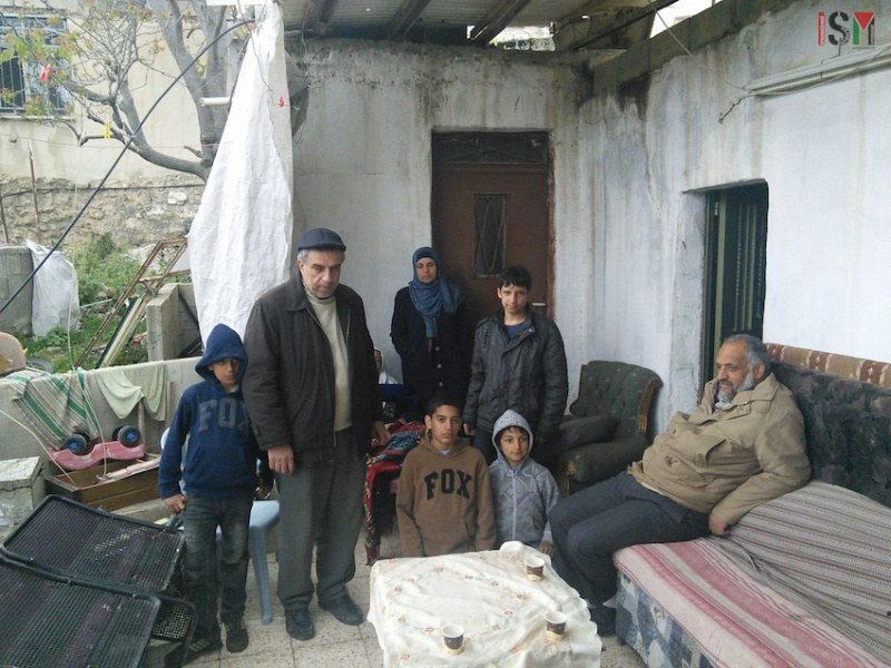 Anggota keluarga Amro berkumpul di samping bagian bangunan rumah mereka yang masih tegak berdiri. Foto: ISM