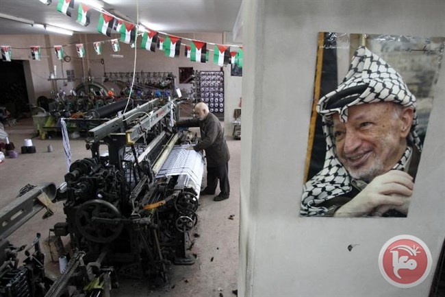 Yasser Al-Hirbawi, pemilik pabrik yang memproduksi keffiyeh hitam putih (penutup kepala tradisional Palestina), berdiri di belakang foto Yasser Arafat, pemimpin Palestina pada 10 Maret 2015 di Al-Khalil. Foto: AFP/Hazem Bader)
