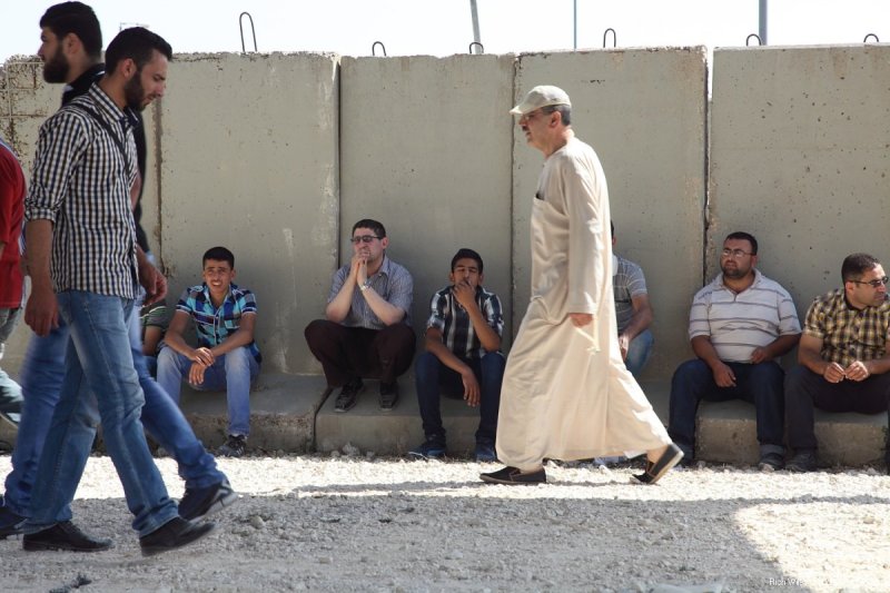 Para lelaki Palestina yang ditolak melintas ke Baitul Maqdis duduk berbaris di tembok yang mengelilingi pos pemeriksaan. Foto: Rich Wiles