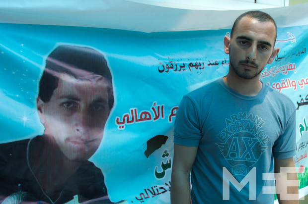Mahmoud berdiri di samping poster saudara kembarnya, Mohammed. Foto: MEE/Abdel al Qaisi