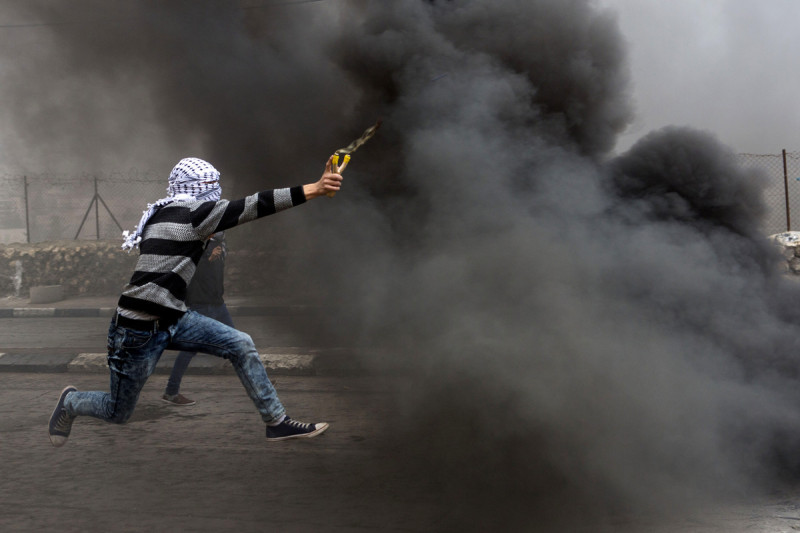 Seorang pendemo Palestina melemparkan batu ke arah para serdadu Zionis yang ada di depan tembok. Foto: Anne Paq