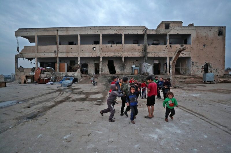 Anak-anak dari keluarga muhajirin yang tinggal di gedung sekolah yang rusak dan terbengkalai, bermain di halaman di daerah Binnish, Idlib, Suriah, 2 Maret 2021. [Omar Haj Kadour/AFP via Getty Images] 