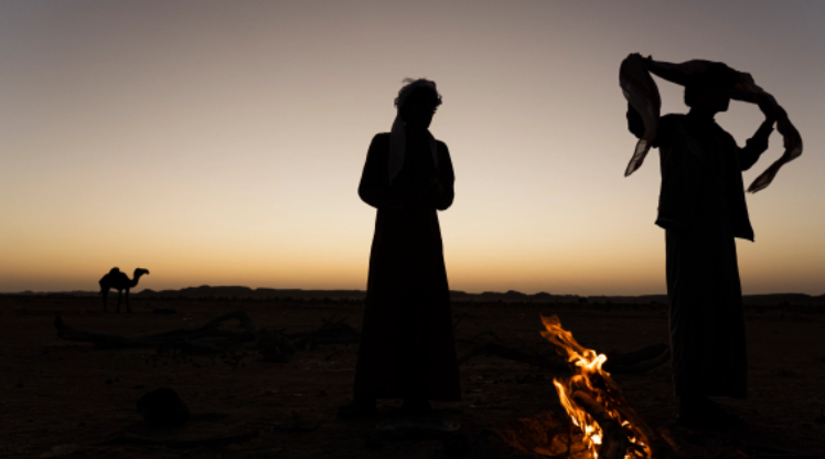 Orang-orang Badui berdiri di sekitar api unggun antara kota Rumah dan 'Empty Quarter'–gurun pasir yang meliputi sepertiga Semenanjung Arab bagian selatan. Di sini, Mahri Badui memelihara unta dan kambing mereka. Mereka berbolak-balik antara kota dan gurun, di mana unta mereka berada di gurun, sedangkan istri, anak-anak, dan kambing mereka berada di kota. [Tariq Zaidi/Al Jazeera]