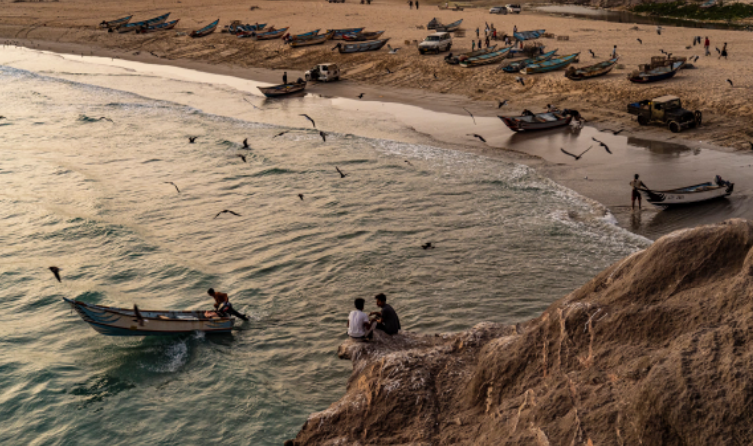 Dua anak laki-laki duduk di bawah tebing sembari menyaksikan perahu nelayan berangkat dari Desa Khyseet, dekat Haswayn. Saat ini masalah terbesar yang dihadapi nelayan bukanlah kekurangan ikan, tetapi krisis bahan bakar yang terjadi di seluruh negeri. Mereka biasa menangkap ikan setiap hari, tetapi sekarang sangat dibatasi oleh pasokan bahan bakar yang semakin menipis. Parahnya lagi, harga peralatan ikut naik drastis karena konflik. [Tariq Zaidi/Al Jazeera]