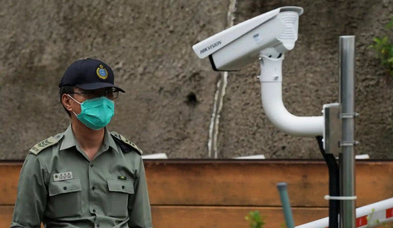 Seorang petugas polisi Cina berdiri di dekat kamera Hikvision di pintu masuk sebuah penjara di Hong Kong. Foto: Lam Yik/Reuters