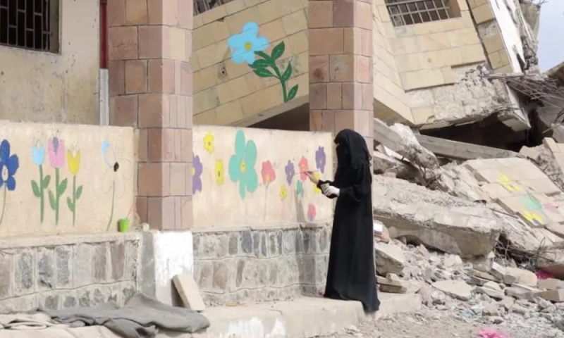 Seorang gadis melukis di tembok sebuah sekolah yang rusak di Yaman barat daya. Foto: Save the Children